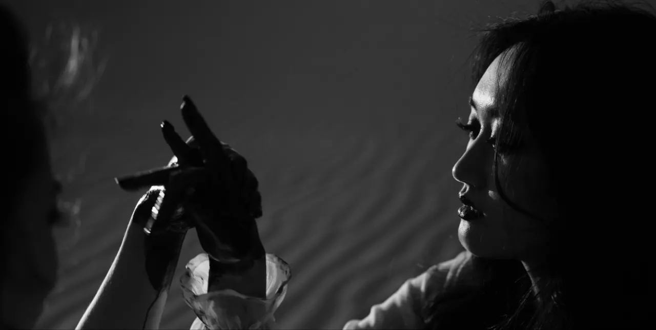 Still from Thin White Material: a cigarette held aloft in profile under hard key light, black and white